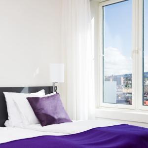 a white bed with a purple blanket and a window at Thon Hotel Panorama in Oslo