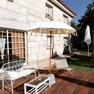 a patio with two chairs and an umbrella and a table at Os Areeiros Turismo Rural & Bodega in Santa Cristina de Cobres