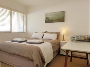 a white bedroom with two beds and a table at 24 Gordonia, Sleeps 7, Beach Front condo - Load-shedding friendly with Solar Power and battery backup in Gordonʼs Bay