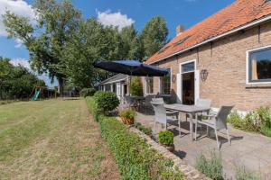 een patio met een tafel en stoelen en een parasol bij Landelijk gelegen familieboerderij in Oudelande