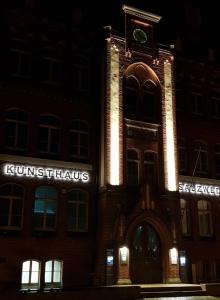 un grand bâtiment en briques avec une tour d'horloge la nuit dans l'établissement Gasthaus Kristall, à Salzwedel