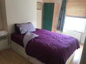 a bed in a bedroom with a purple comforter and a window at 295 Sturry Rd in Kent