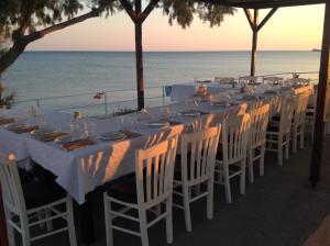 a long table with white chairs and the ocean at Kefalonia Beach Hotel & Bungalows in Lixouri