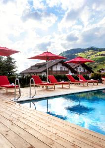 una piscina del complejo con sillas y sombrillas rojas en Hotel Tyrol en Selva di Val Gardena