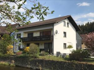 a white house with a balcony and a river at Ferienhaus 1 An der Rodach in Steinwiesen
