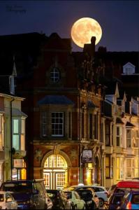 a full moon rising over a building with cars parked at Castle Hotel in Aberystwyth