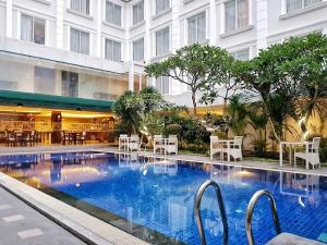 a hotel swimming pool with tables and chairs and a building at LYNN Hotel by Horison in Yogyakarta