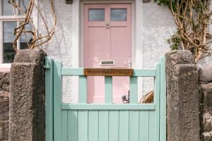 eine rosa Tür an einem Haus mit einem Zaun in der Unterkunft Maggie Puddle Cottage in Grange Over Sands