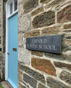 um sinal na lateral de um edifício de tijolos com uma porta azul em The Old Sunday School em Helston