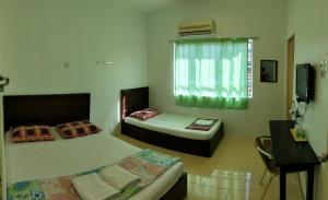 a bedroom with two beds and a desk and a window at Hotel Tanjong in Tanjung Malim