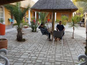 zwei Männer sitzen an einem Tisch auf einer Terrasse mit Schwänen in der Unterkunft Bonjour Inn Palapye in Palatswe