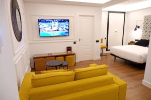 a living room with a yellow couch and a bed at Hotel Colón Plaza in Valladolid