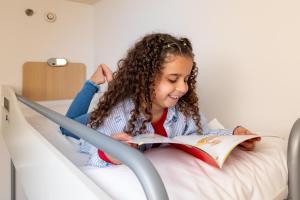 a little girl sitting in a hospital bed reading a book at ibis budget SP Frei Caneca in Sao Paulo