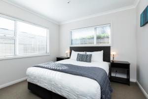 a white bedroom with a large bed and two windows at Beach Street Motel Apartments in New Plymouth