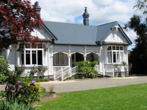 a white house with a porch and flowers at White Elephant Accomodation in Motueka