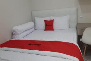 a white bed with a red pillow on it at RedDoorz Syariah near UNSOED in Purwokerto
