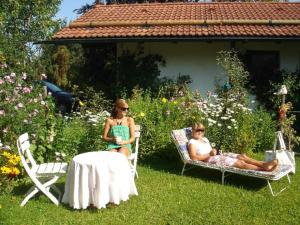 twee vrouwen zittend op stoelen en een tafel in een tuin bij Ferienwohnung Burgenblick in Hopferau