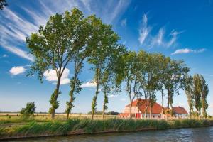 una fila de árboles y una casa roja junto a un río en Maenhoudthoeve met zwembad en sauna en Oudenburg