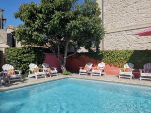 a swimming pool with chairs and a tree next to a building at Hôtel Sous les Figuiers - Piscine, parking, centre ville in Saint-Rémy-de-Provence