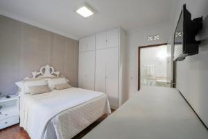 a bedroom with a white bed and a television at Casa de Maria Suítes in Recife