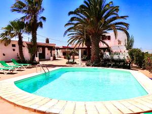 una gran piscina con palmeras y una casa en Villa NARE - Casa típica majorera, en Villaverde