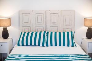 Cama blanca con almohadas de rayas azules y blancas en Casas Burnay I, en Ericeira