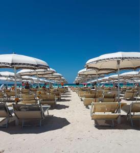 una fila di sedie e ombrelloni in spiaggia di Hotel Salento Mirfran a Torre San Giovanni Ugento