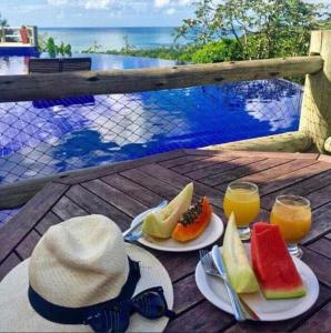 a table with two plates of fruit and two glasses of juice at Bangalô Villas do Pratagy com jacuzzi in Maceió