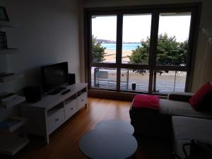 ein Wohnzimmer mit einem Sofa, einem TV und einem Fenster in der Unterkunft Apto. Vista Playa Poniente in Gijón