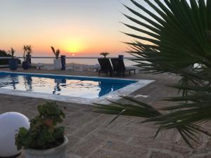 ein Pool mit Stühlen und ein Sonnenuntergang im Hintergrund in der Unterkunft LES OLIVIERS in Oualidia