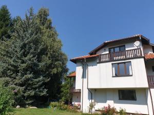 a white building with a balcony and a tree at Guest House Ela in Dolna Banya