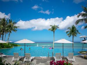 a pool with chairs and palm trees and the ocean at HOTEL MOON BEACH MUSEUM RESORT in Onna