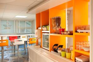 a kitchen with orange and yellow cabinets and chairs at Premiere Classe Bordeaux Sud - Pessac Becquerel in Pessac