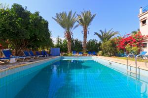 a swimming pool with blue chairs and palm trees at Follow The Sun Hotel Apartments in Polis Chrysochous