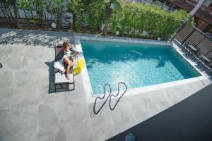 a woman sitting on a chair next to a swimming pool at Olympus Thalassea Boutique Hotel in Paralia Katerinis