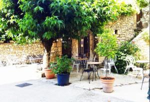 een patio met tafels, stoelen en bomen bij Auberge du Puits in Souillac