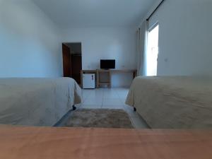 ein weißes Zimmer mit zwei Betten und einem Fernseher in der Unterkunft Hotel Samambaia in Indiara 
