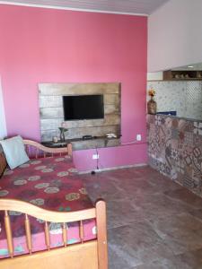 uma sala de estar com paredes cor-de-rosa, uma mesa e uma televisão em Chalé e suite Manu em Ilhabela