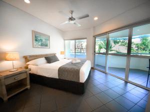 a bedroom with a bed with a ceiling fan and windows at Beach Terraces in Port Douglas +46 photos