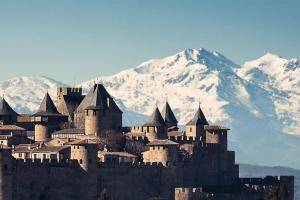 a large castle with snowy mountains in the background at Ruby - Gîte 2 chambres dans vieux prieuré près de Carcassonne in Sainte-Eulalie