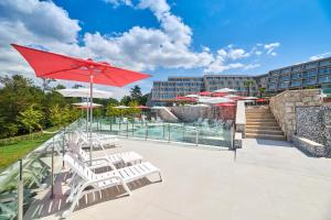 a patio with chairs and a pool with a red umbrella at Hotel Mediteran Plava Laguna in Poreč