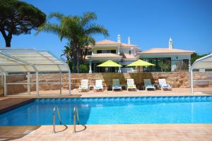 a swimming pool with chairs and umbrellas in front of a house at Villa Fonte Santa in Quarteira