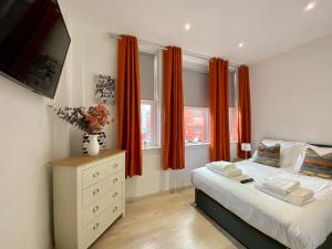 a bedroom with orange curtains and a bed and a dresser at Princess Theatre Beach View Apartments by Blackpool Service Apartments in Blackpool