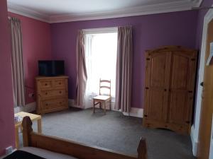 1 dormitorio con paredes moradas, ventana y silla en The Waverley Guest House, en Dumfries
