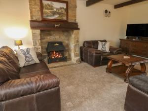 sala de estar con muebles de cuero y chimenea en Hill Top Cottage, en Keighley