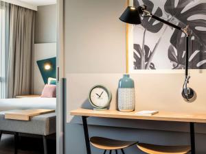 パリにあるAparthotel Adagio Paris Nationのデスク、時計、ベッドが備わる客室です。