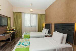 a hotel room with two beds and a desk at Oasis Deira Hotel in Dubai