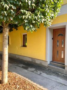 ein gelbes Gebäude mit einer Holztür und einem Baum in der Unterkunft Árvíz Apartman in Szeged