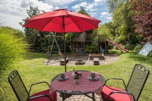 einen Tisch mit einem roten Regenschirm und einem Spielplatz in der Unterkunft Ferienwohnung Lilian in Meckenbeuren