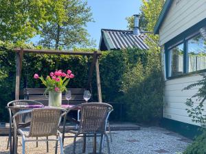 een tafel met stoelen en een vaas met roze bloemen bij Ferienpark Vislust Ferienhaus Balu mit eigenem Steiger zum angeln Ijsselmeer Niederlande in Wervershoof